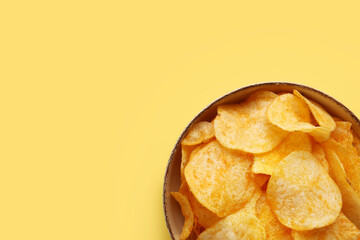 Bowl with delicious potato chips on yellow background