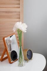 Vase with ranunculus flowers, alarm clock and mirror on table in bedroom