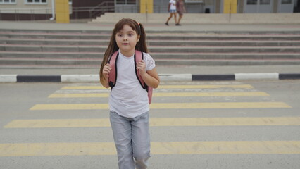girl child goes through pedestrian crossing. happy student with school backpack. zebra road. child...