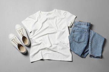 Stylish t-shirt, jeans and sneakers on light grey background, flat lay