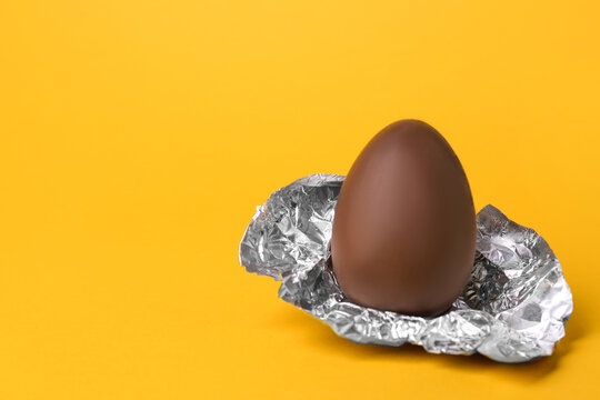 Tasty chocolate egg with foil on orange background. Space for text
