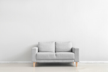 Stylish grey sofa near white wall