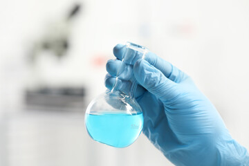 Scientist holding flask of light blue liquid in laboratory, closeup