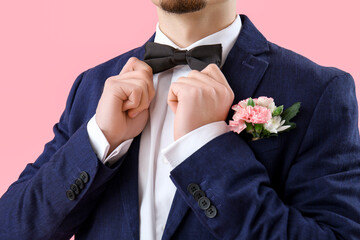 Young guy in prom suit adjusting bowtie on pink background, closeup