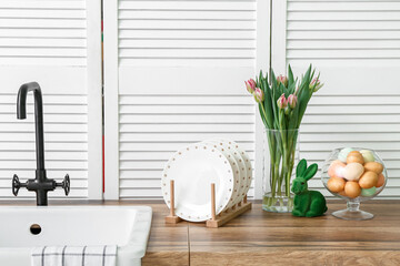 Easter eggs, bunny, tulip flowers and sink on white kitchen counter