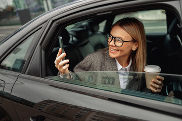 Happy woman passenger taking photo of attractions from car back seat when traveling in city taxi