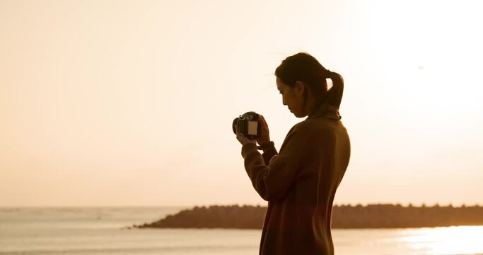 Woman use digital camera to take photo at the beach in sunset time