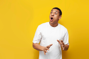 young shocked african american guy in white oversized t-shirt is surprised on yellow isolated background - obrazy, fototapety, plakaty