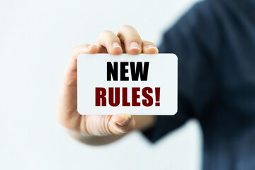 New rules text on blank business card being held by a woman's hand with blurred background. Business concept about new rules.