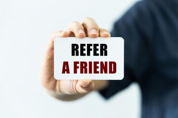 Refer a friend text on blank business card being held by a woman's hand with blurred background. Business concept to inform audience to refer a friend.