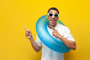 cheerful african american guy in sunglasses with inflatable swim ring shows his hands to side on yellow background - obrazy, fototapety, plakaty