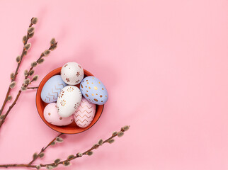 A bowl of easter eggs with a branch of willow on a pink background.