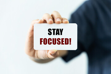 Stay focused text on blank business card being held by a woman's hand with blurred background. Business concept to inform audience to stay focused.