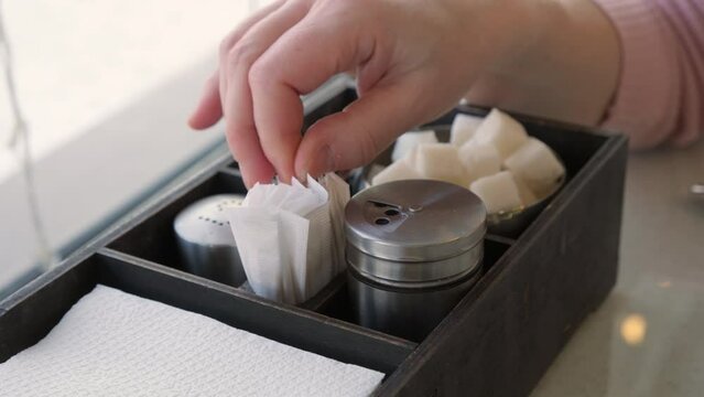 Hand takes toothpick in individual package from wooden box on table in cafe 