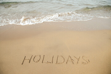 Holidays lettering on the beach with wave and clear blue sea. 