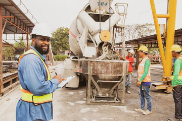 African American foreman inspects the pouring of mortar from a ready-mixed cement truck by team of...