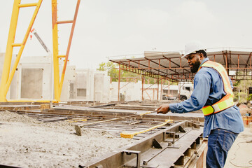 Fototapeta premium African American male lead architect diligently uses builder's tool to spread cement poured into a solidly defined structural block for prefabrication in an outdoor construction yard.