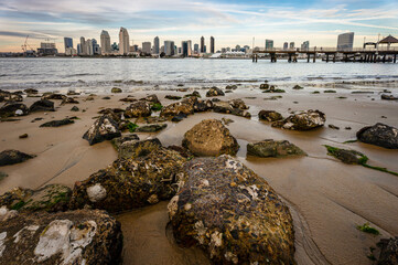 San Diego, California skyline seen from Coronado Island with beach and rocks at dusk