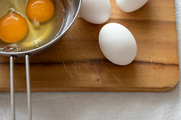 カッティングボードにのった生卵とボールに入った割られた生卵
