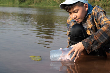 Asian schoolboy holding transparent plastic tube to keep freshwater algae from local river inside...
