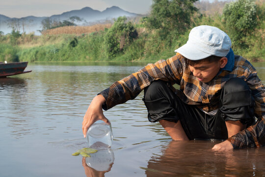 Asian schoolboy holding transparent plastic tube to keep freshwater algae from local river inside to study the fertility of the river's nature and to do environment school project work, in motion.