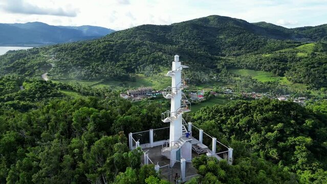 Breathtaking Aerial View of White Lighthouse atop mountain in lush rainforest with vast sea and clouds in background. Bato, Catanduanes, Philippines.