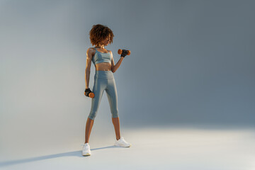Athletic woman doing exercise with weight dumbbells on studio background. Strength and motivation