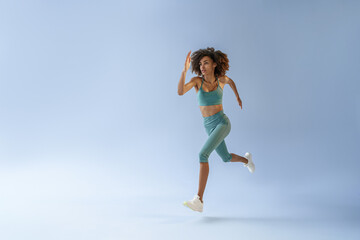 Determined sporty woman running in Mid-Air exercising during cardio workout over studio background