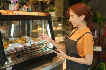 Caucusian woman entrepreneur using digital tablet while standing in front of the counter in cozy coffee shop interior..
