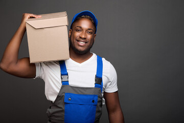 Cheerful loader easily carries weights in a box on his shoulder holding only one hand. Against gray...
