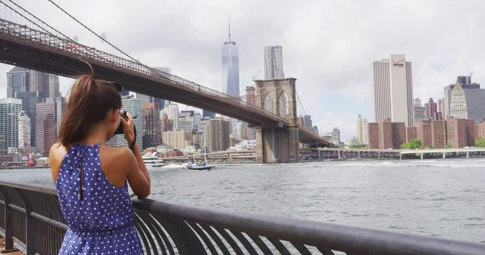 Tourist taking travel picture of Brooklyn bridge and New York City skyline with camera during summer holidays. Unrecognizable female young adult enjoying USA vacations in blue dress
