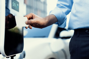 Hand holding credit card to pay public charging station and recharge her electric vehicle,...