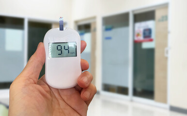 Image closeup of hand hold Blood Glucose Monitoring meter to test Diabetes mellitus by checking Fasting Blood Sugar (FBS) value for healthcare business background.