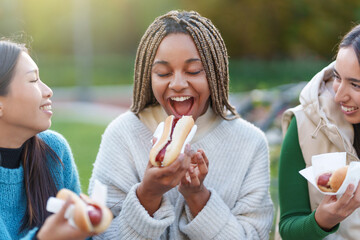 Friends eating hot dogs in a park