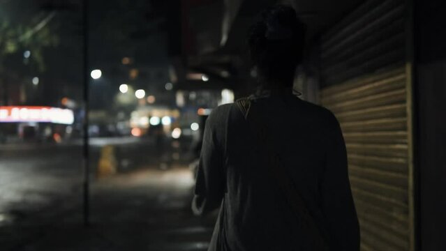 Woman walking in city nighttime slow motion bokeh lights illuminated shop signs