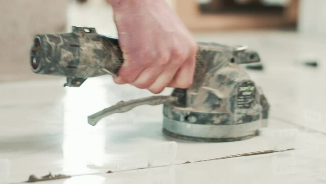 Builder installing tiles on the floor with a tile vibrator machine.