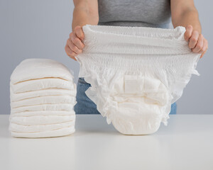A woman chooses an adult diaper from a pile. Urinary incontinence problem. - obrazy, fototapety, plakaty