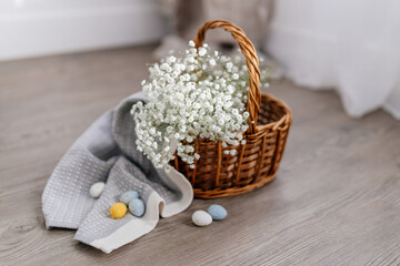 Obraz na płótnie Canvas A basket of twigs with white flowers, a towel, blue, yellow, white eggs. Spring Background for Easter