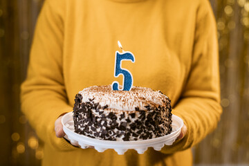 Birthday 5. Woman holding birthday cake with burning candles number 5 against decorated background,...