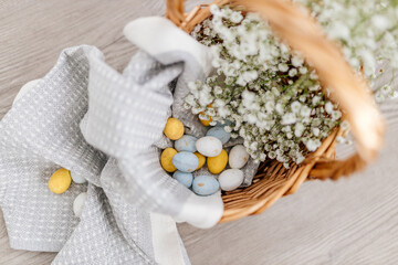 Blue, yellow, white eggs and white small flowers lie in a basket close-up. Spring Background for Easter