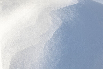 a mountain of white snow with waves from the wind sparkles in the sun