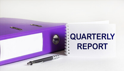 A folder with documents, a pen and a notepad with the text QUARTERLY REPORT on a white background
