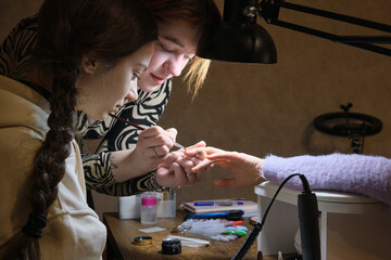 A young woman mentor teacher coach conducts individual training in manicure techniques.