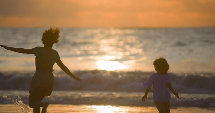 A child and family friend play on beach in sunset. A game of catch-up on beach. A boy runs after woman, his close friend on vacation by sea. A woman plays with a small child as if she were her own.