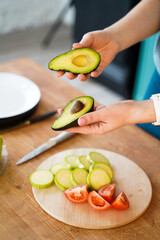 a girl in the kitchen holds a sliced bright green avocado in her hands