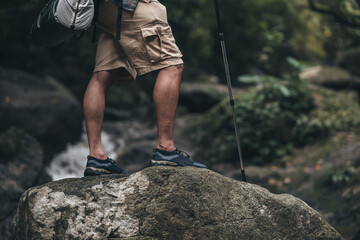 Hikers use trekking pole with backpacks walking through the rock and water on stream in the forest. hiking and adventure concept.