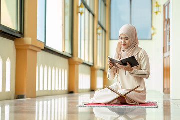 The image of an Asian Muslim woman in the Islamic religion in hijab in cream color. Sitting reading...