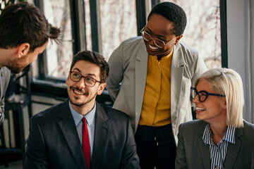 A mixed group of business people sitting and standing around a table and talking. Business people checking reports.