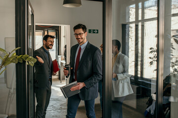 Shot of a group of a businessman holding the door while his coworkers enter the office. Confident young business people working together in the office.