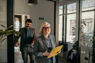 Smiling business people in a suit open an office door, holding a tablet and entering in office.